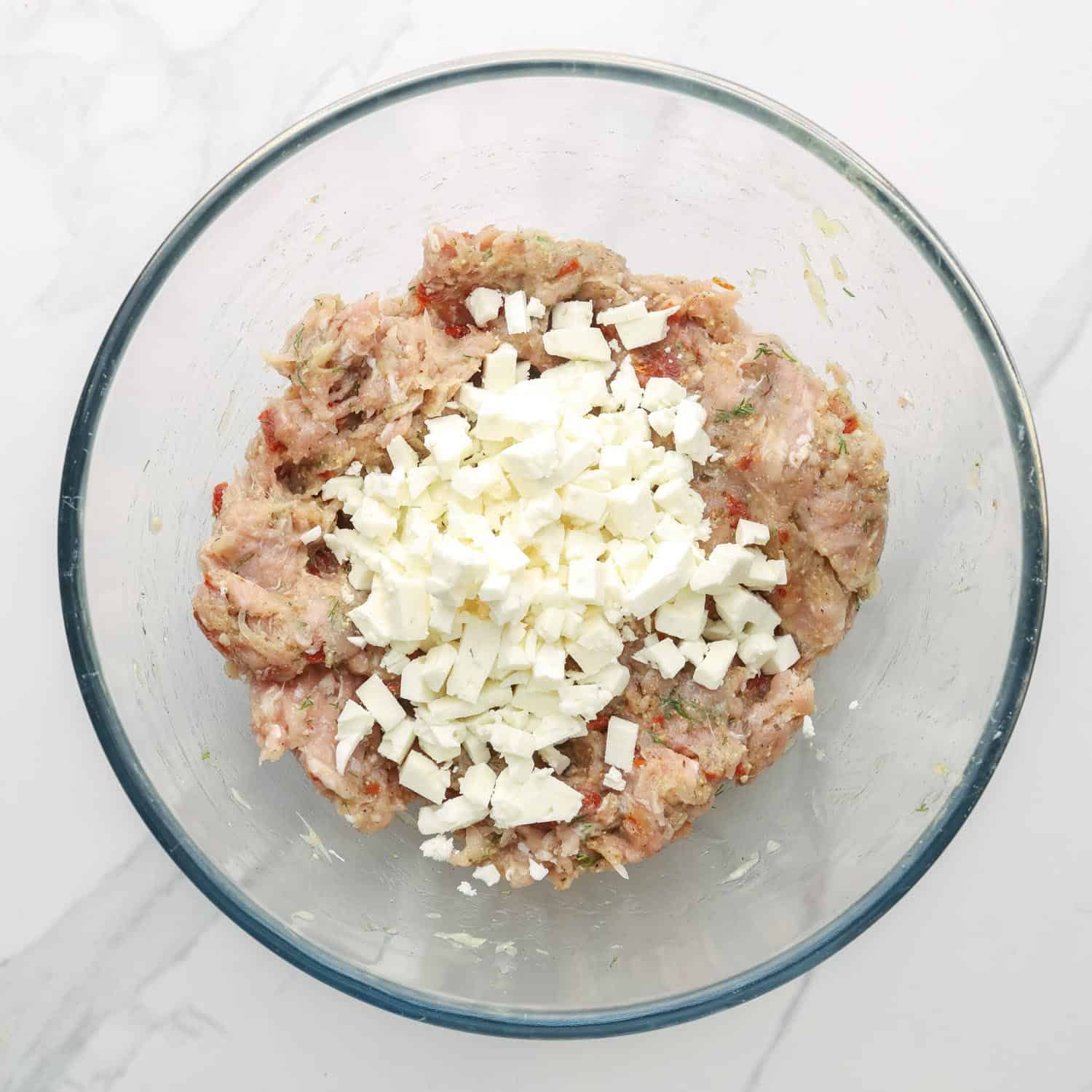 crumbled feta added to chicken burger mixture in a glass mixing bowl.