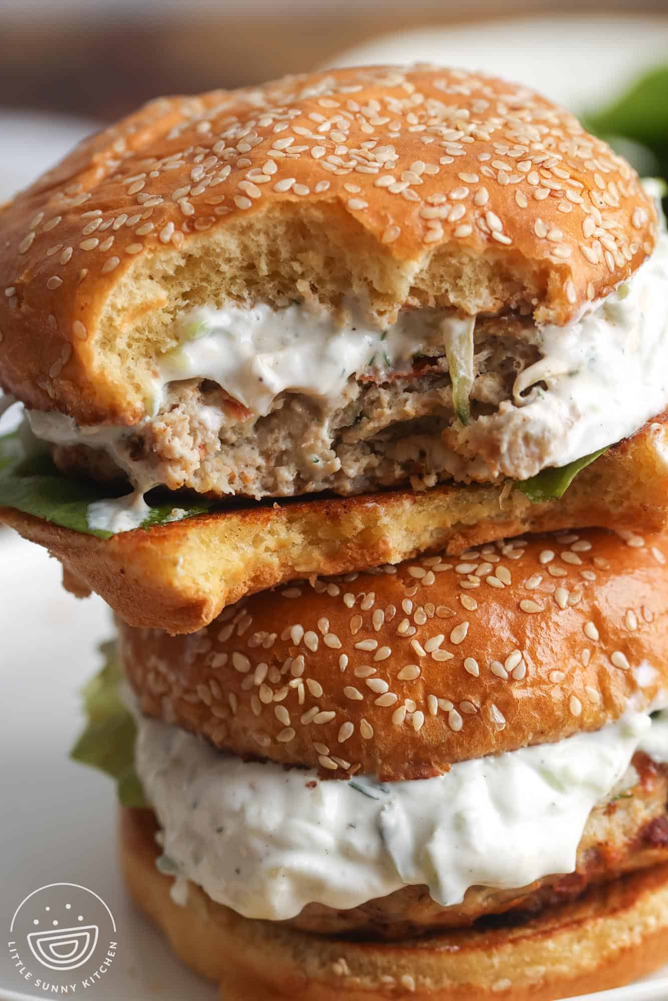 two greek chicken burgers stacked on top of each other. One has a bite taken.