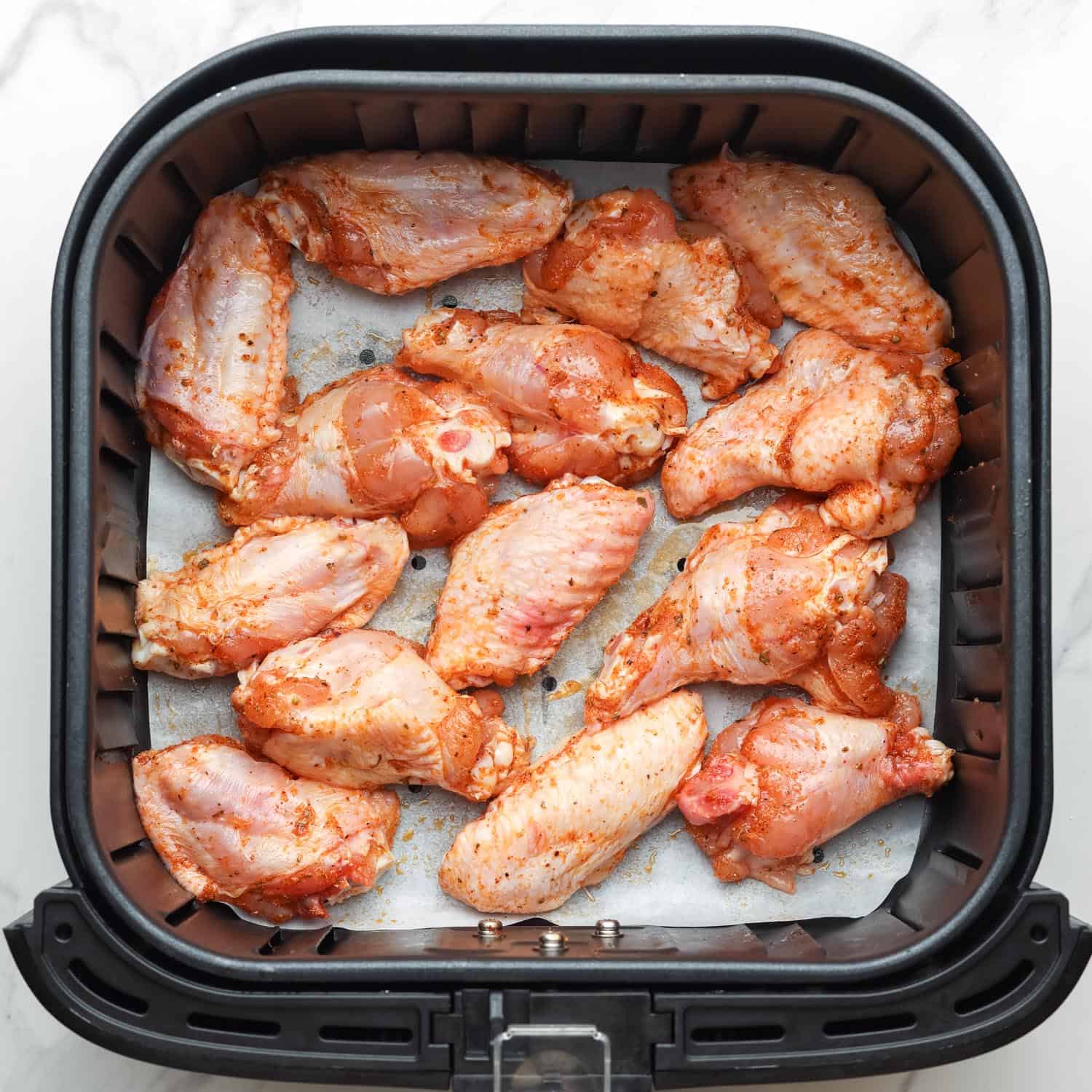 Raw chicken wings in a square air fryer basket on top of a parchment paper air fryer liner.