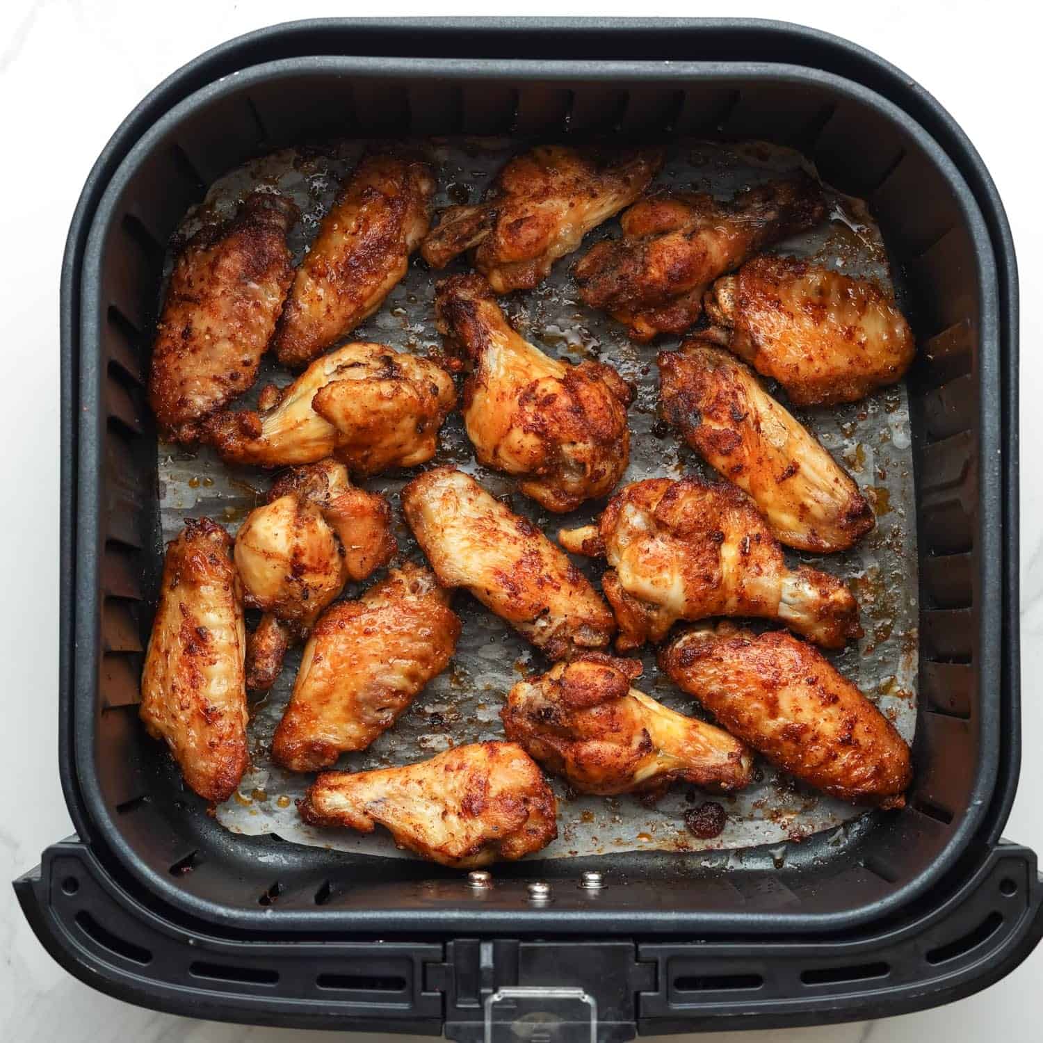 crispy browned air fryer chicken wings in a parchment lined square air fryer basket.