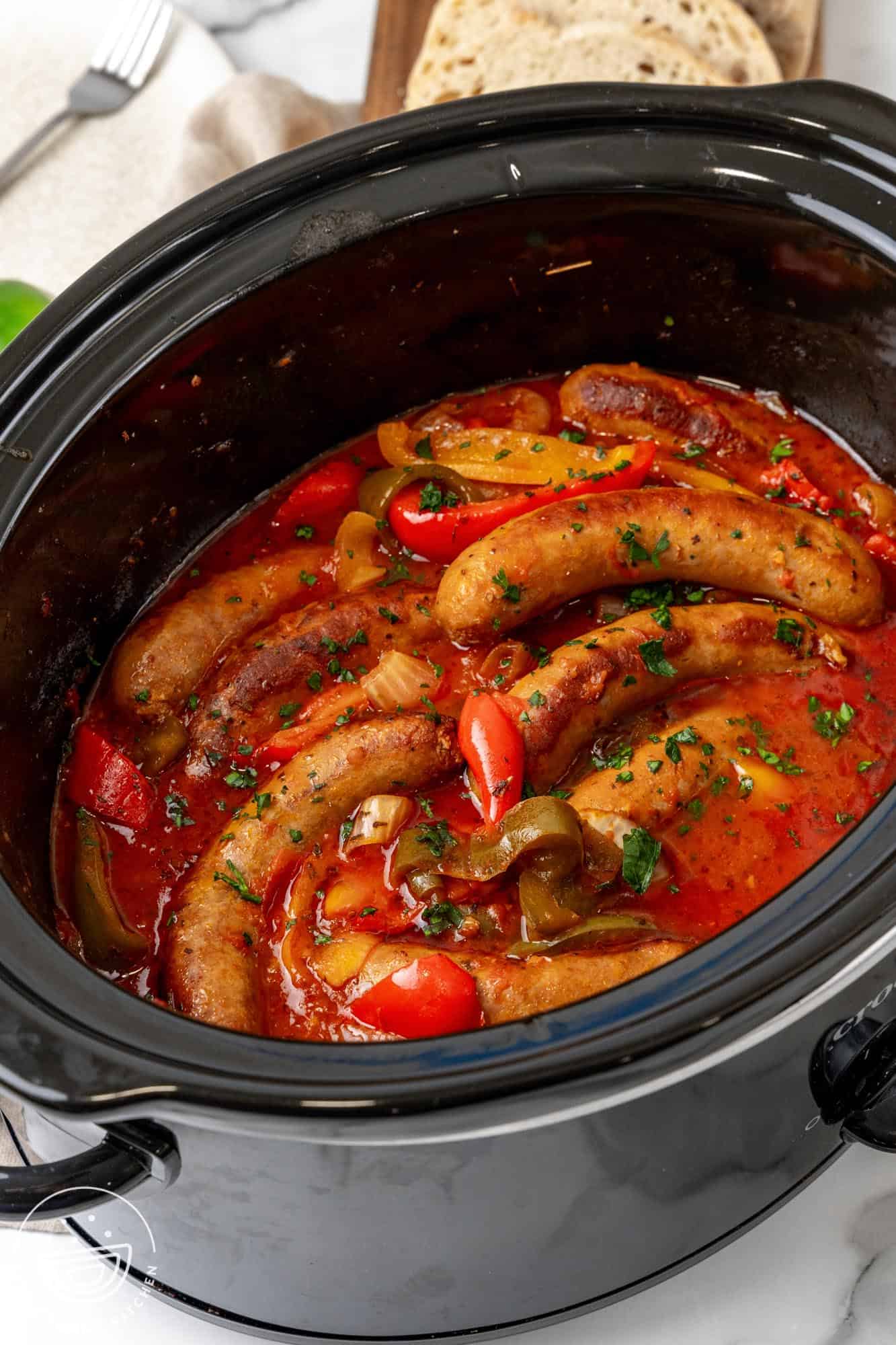 a black slow cooker filled with italian sausage and peppers.