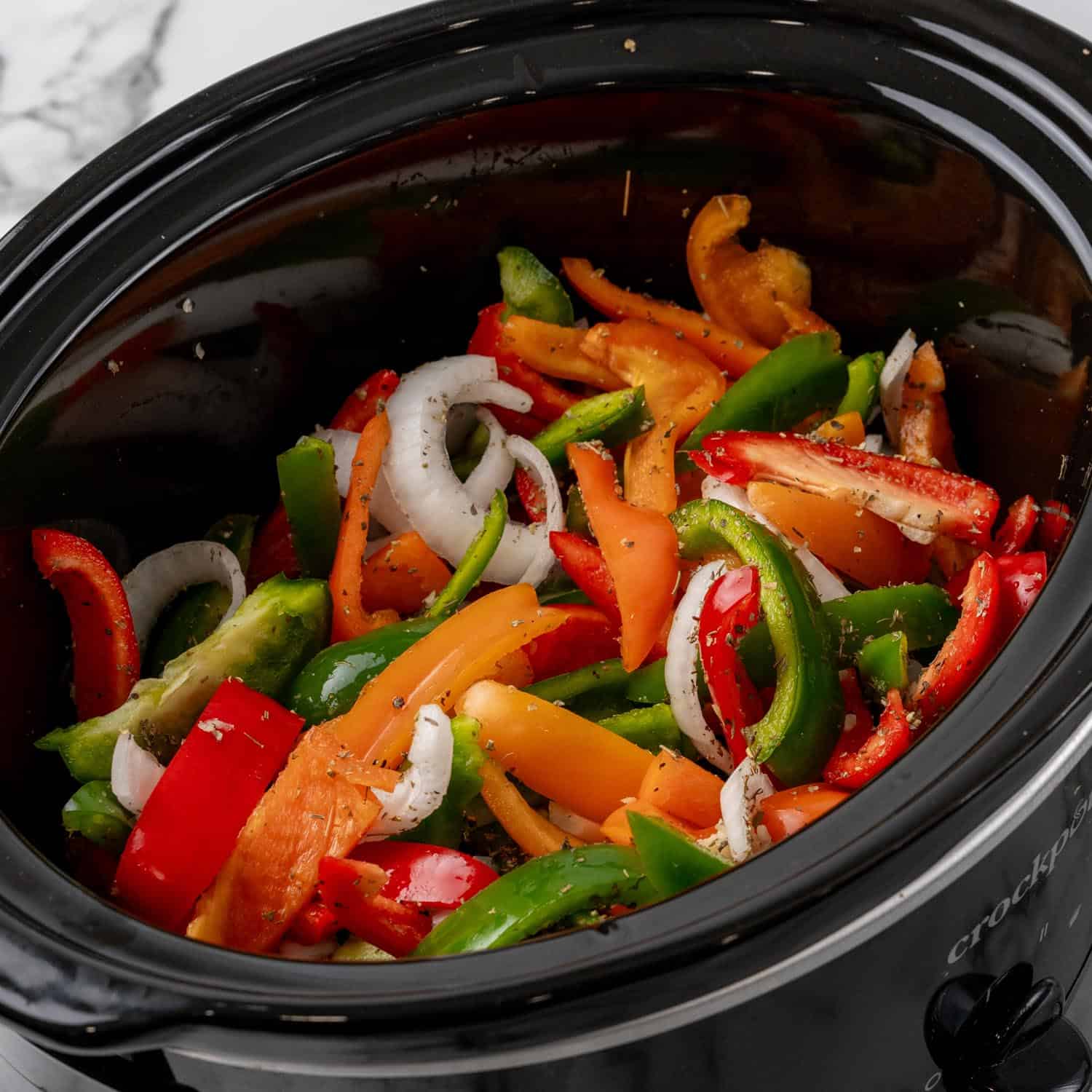 seasoned fresh bell pepper strips and onion slices in a crock pot.