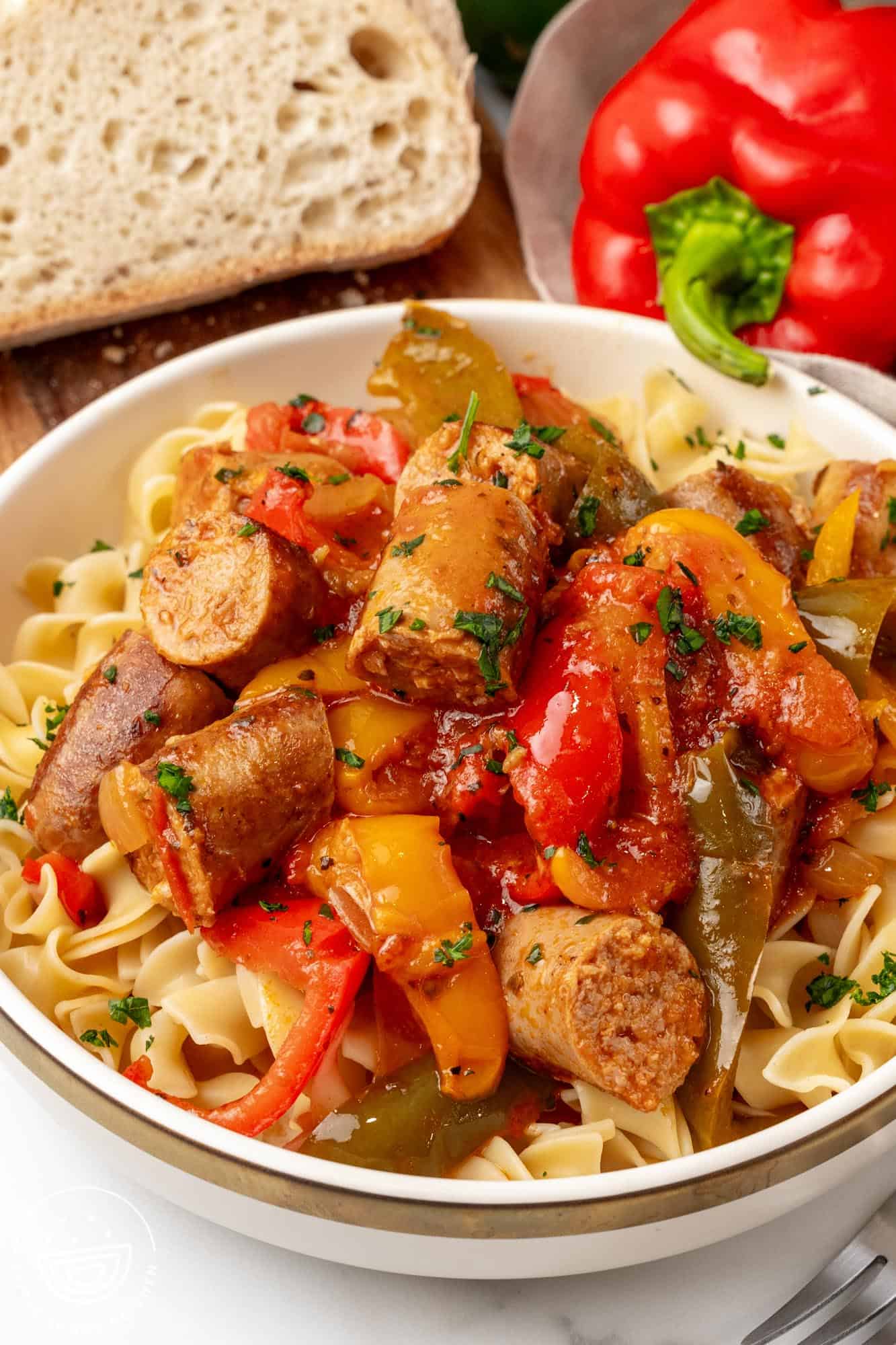 a bowl of egg noodles topped with slow cooker peppers and sausage.