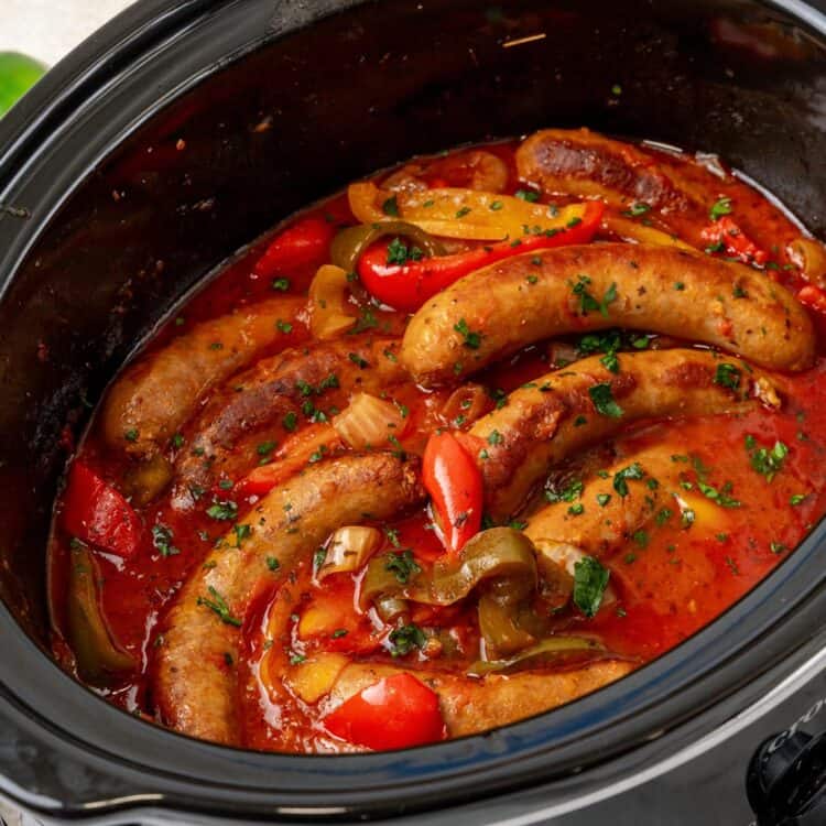 a black slow cooker filled with italian sausage and peppers.