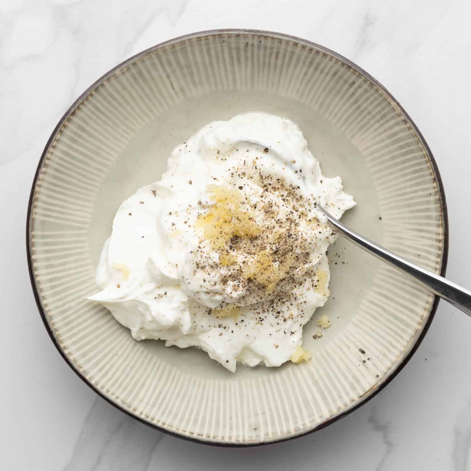 A bowl of greek yogurt with garlic and seasonings added.