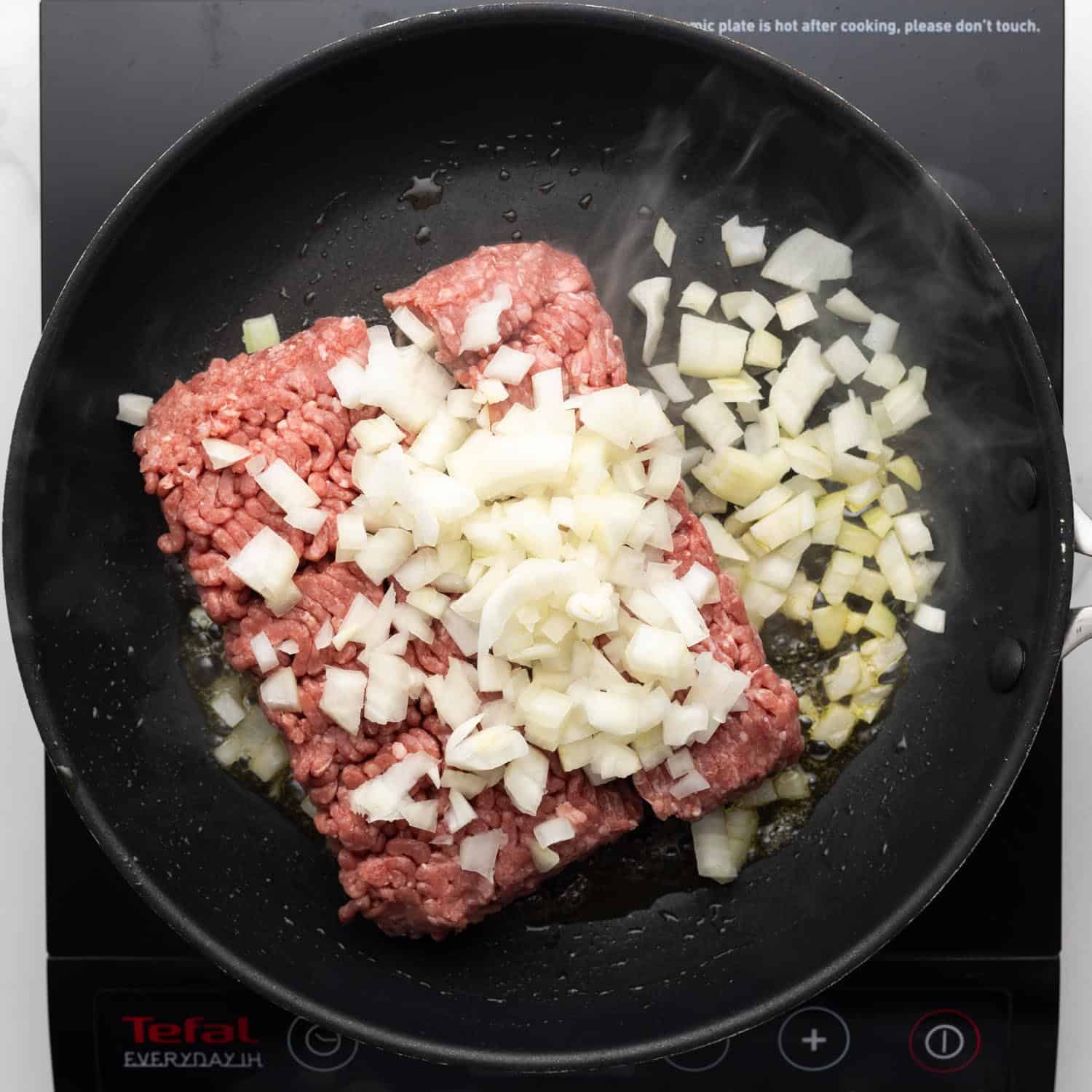 A pound of ground beef in a skillet with chopped onion.