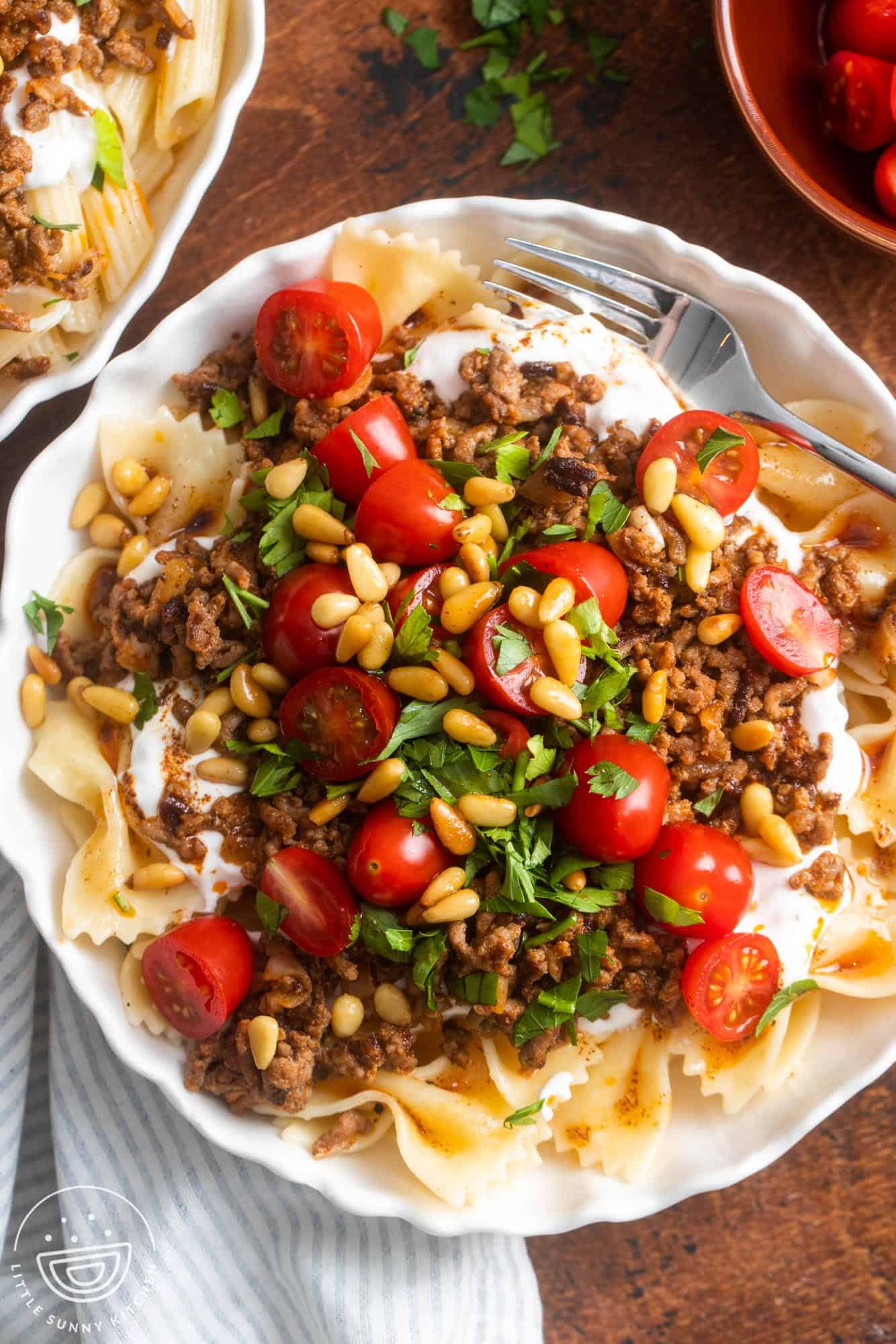 Overhead view of a large bowl of Turkish Pasta. The buttery bow tie noodles are topped with garlicky yogurt, ground meat, tomatoes, and pine nuts.