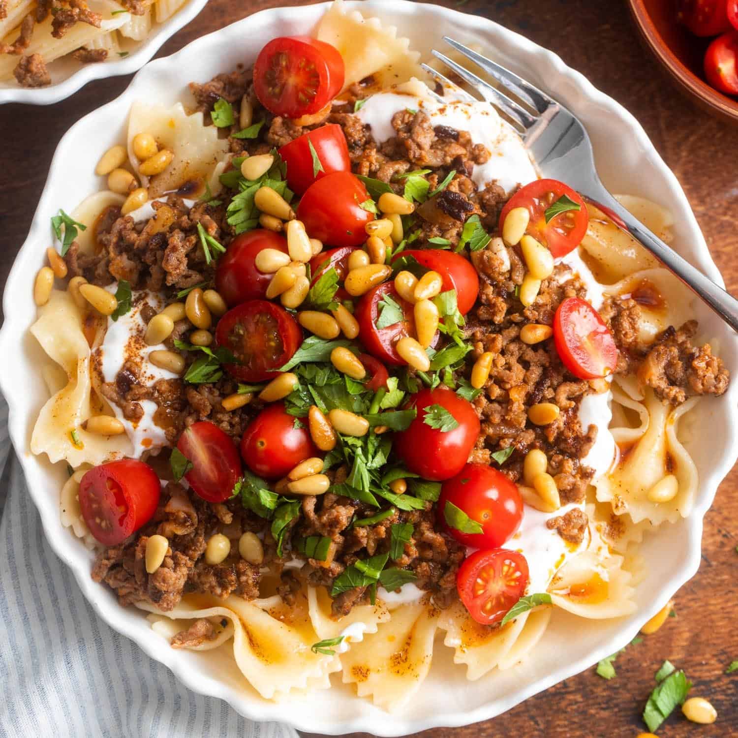 An assembled bowl of turkish pasta with meat sauce, yogurt, tomatoes, and pinenuts. 