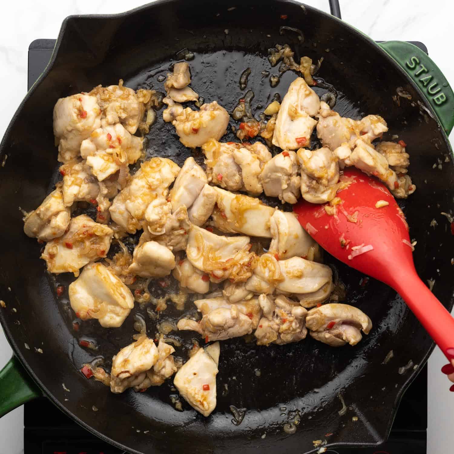 Cubed dark meat chicken in a cast iron skillet with shallots, garlic, and chili peppers.