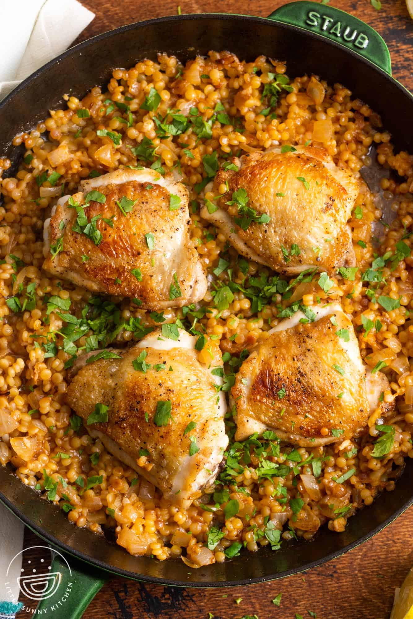 a cast iron skillet of couscous with four chicken thighs on top.