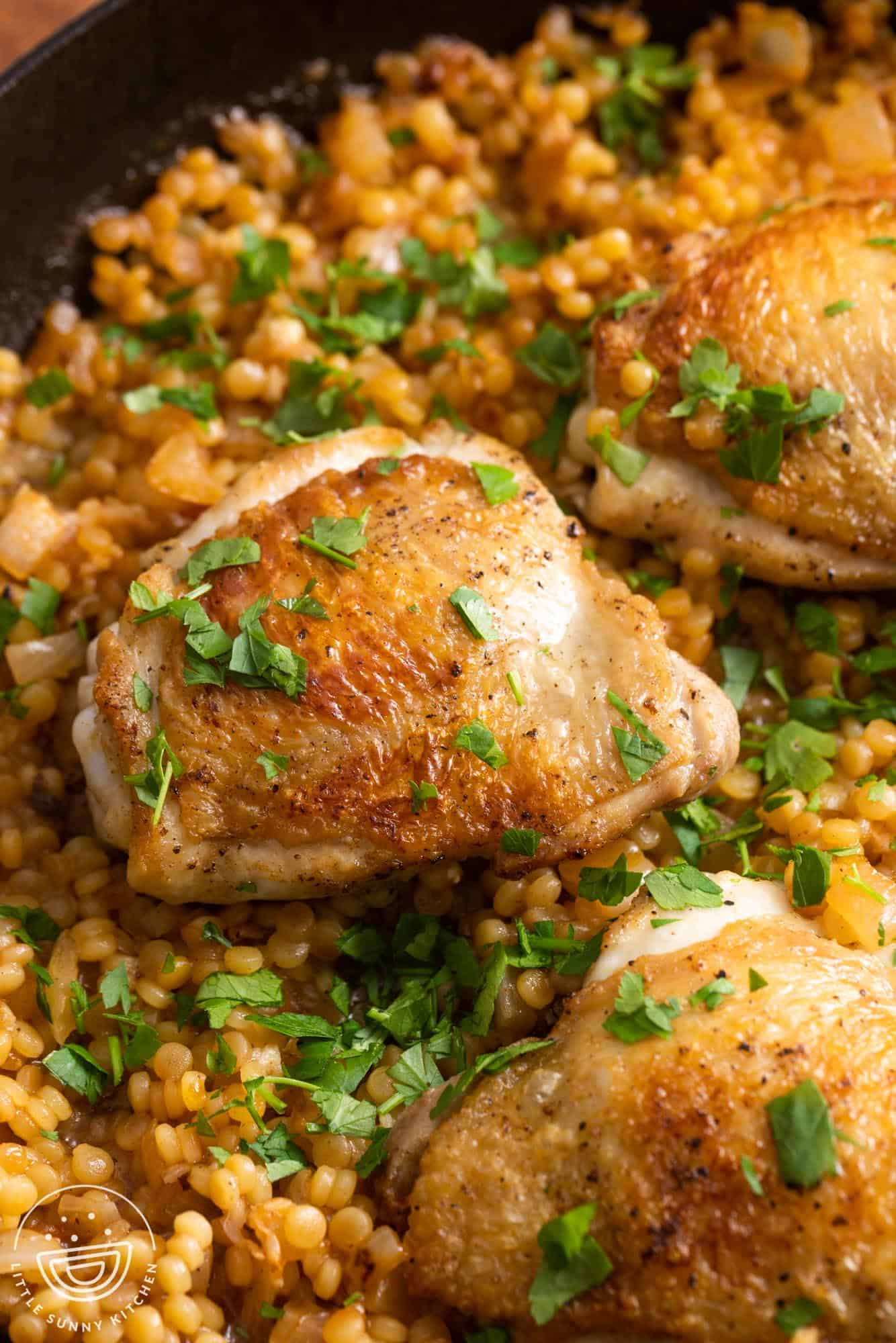 crispy chicken thighs on top of couscous, garnished with chopped parsley.