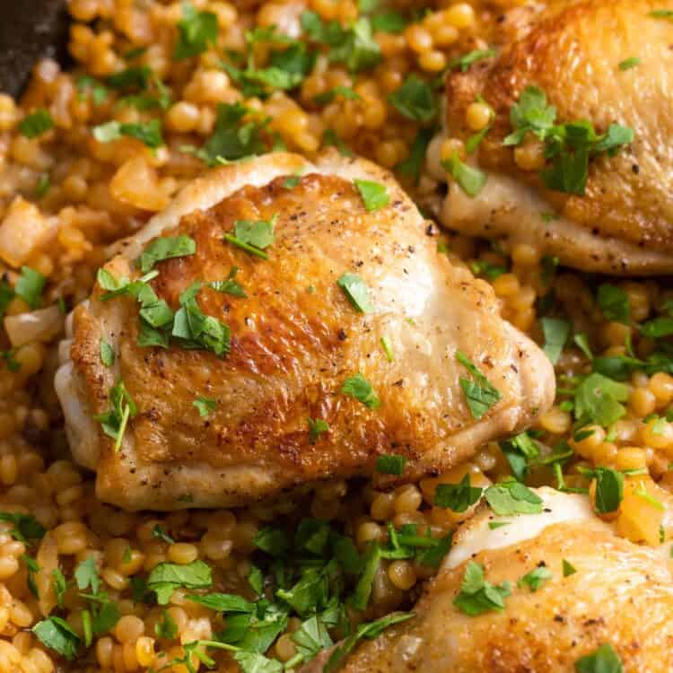 crispy chicken thighs on top of couscous, garnished with chopped parsley.