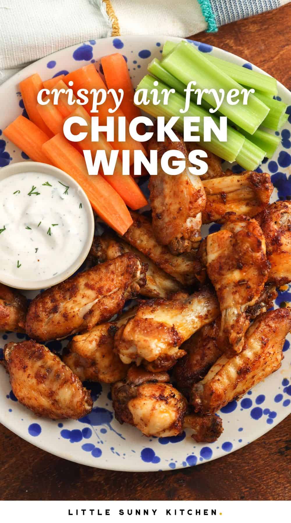 a blue and white spotted plate holding seasoned air fryer chicken wings with a side of ranch, carrot sticks, and celery sticks. Text overlay says 