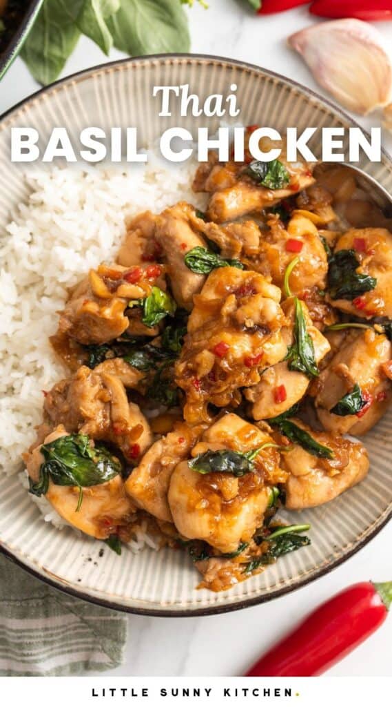 a ceramic bowl of rice topped with thai basil chicken. Around the bowl are chili peppers, garlic cloves and fresh thai basil. Text overlay says 