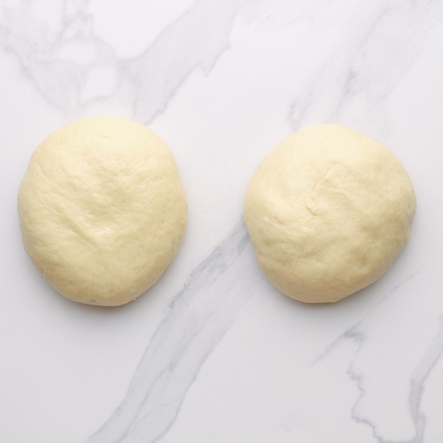 two portions of ramadan bread dough rolled into balls, resting on a marble surface. 