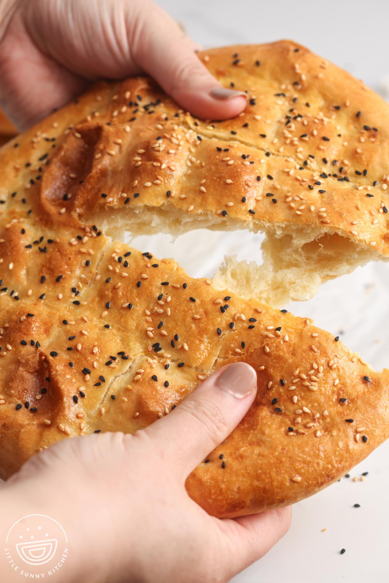 hands pulling apart a round loaf of turkish ramadan bread. 