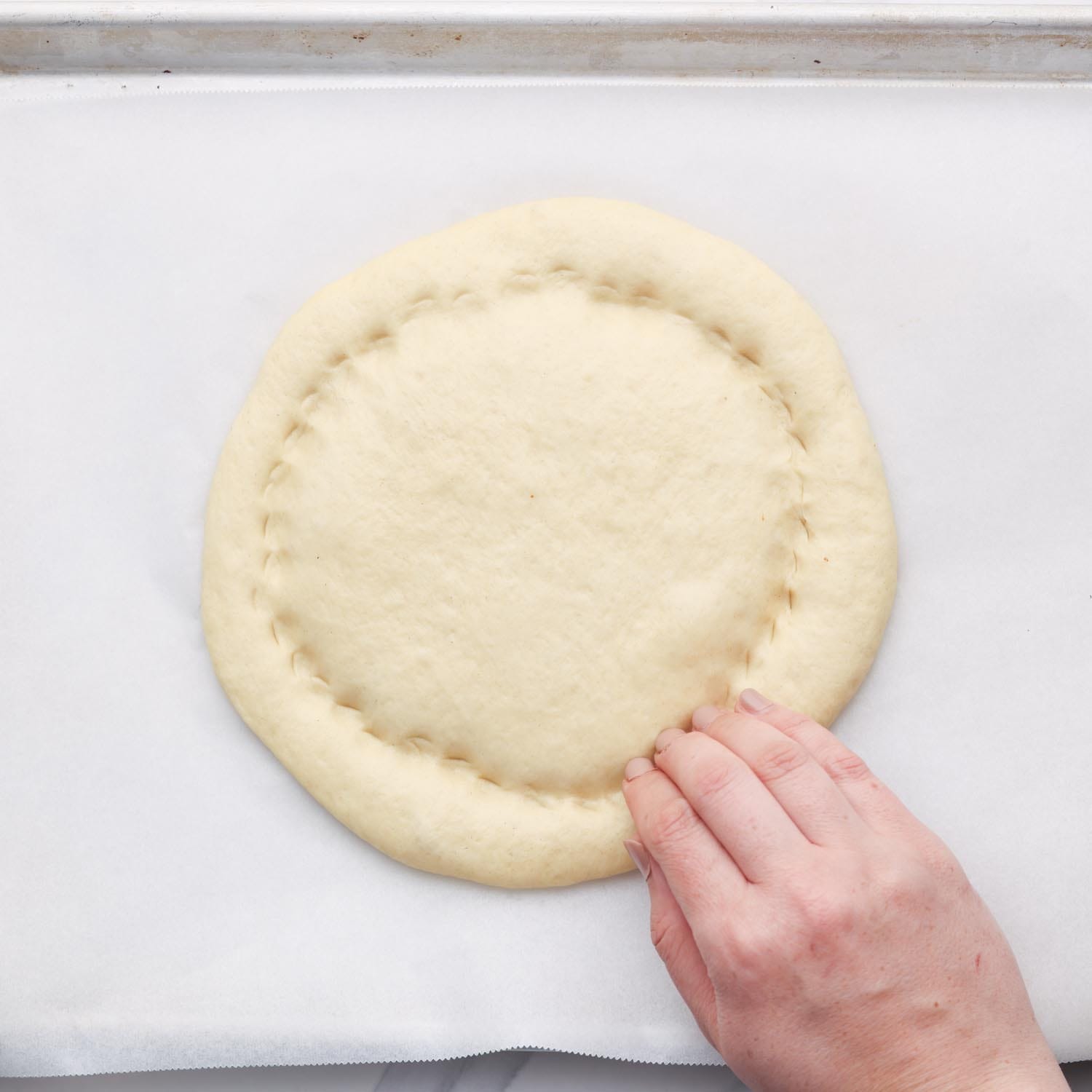 a hand using fingers to create a round inner outline in a round flat bread loaf. 