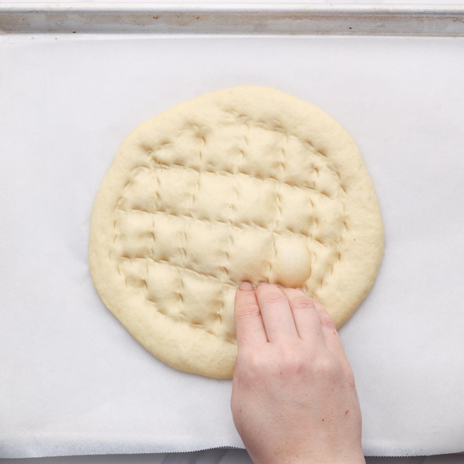 a hand making pillowy shapes in a loaf of ramadan bread with fingers. 