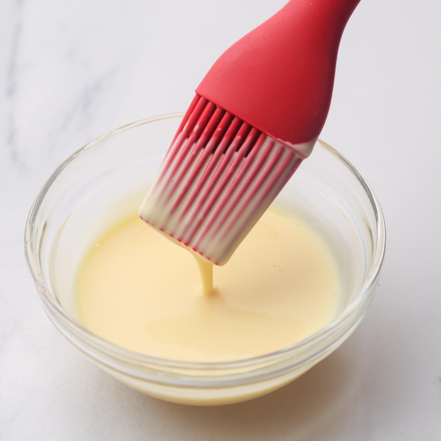 egg wash mixed in a glass ramekin, a red silicone brush is dipping in.