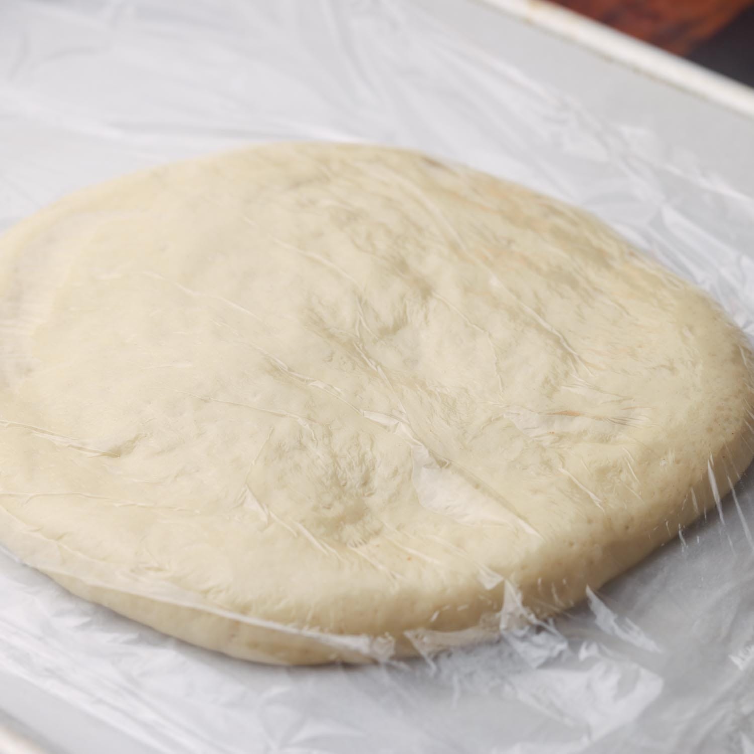 dough for pidesi in a round shape, covered with plastic wrap