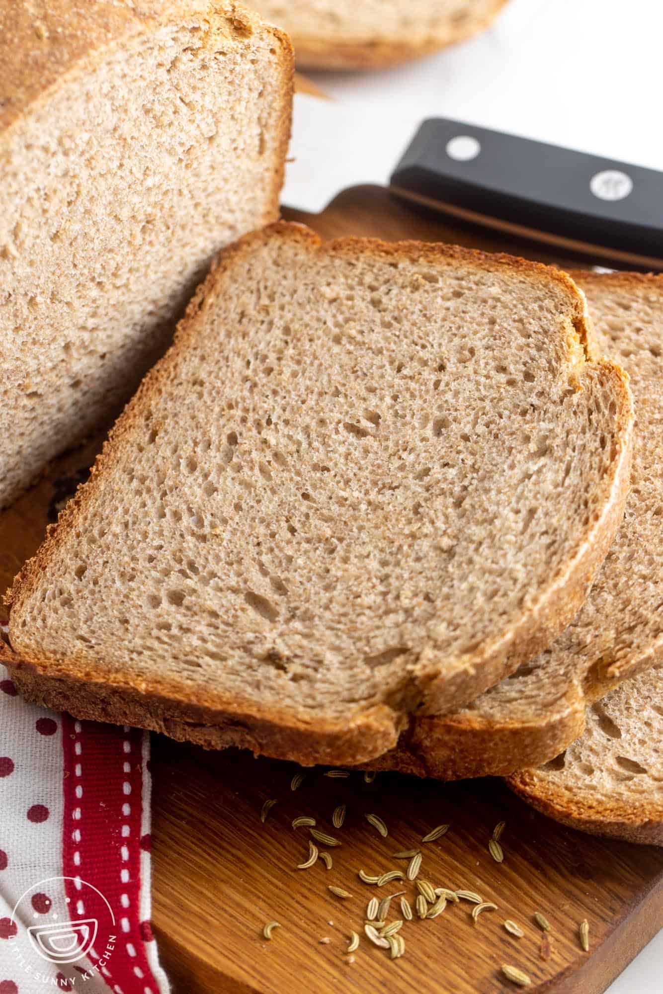 slices of bread machine rye bread on a wooden cutting board. Caraway seeds are sprinkled on the board as well.