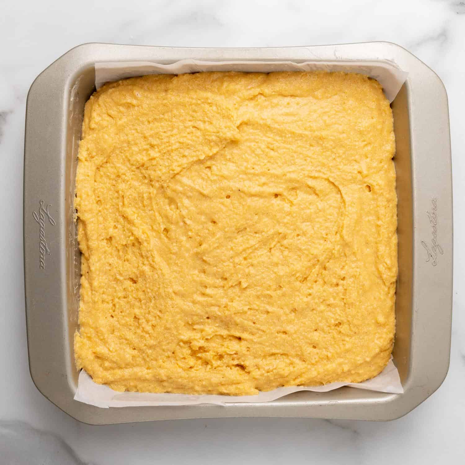 sweet potato cornbread batter in a square metal baking pan lined with parchment paper.