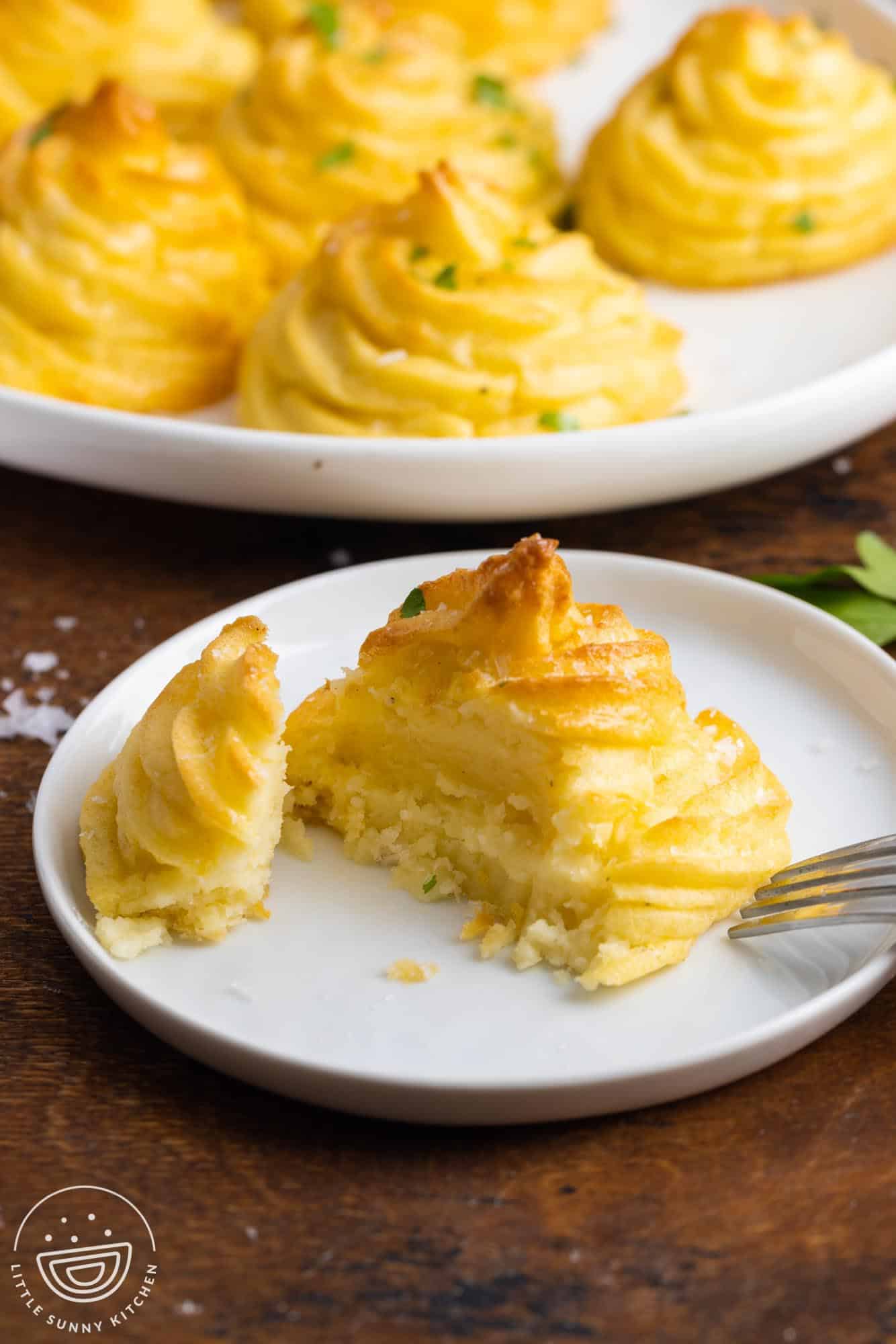 a duchess potato on a small plate, sliced with a fork to show the fluffy inside. 