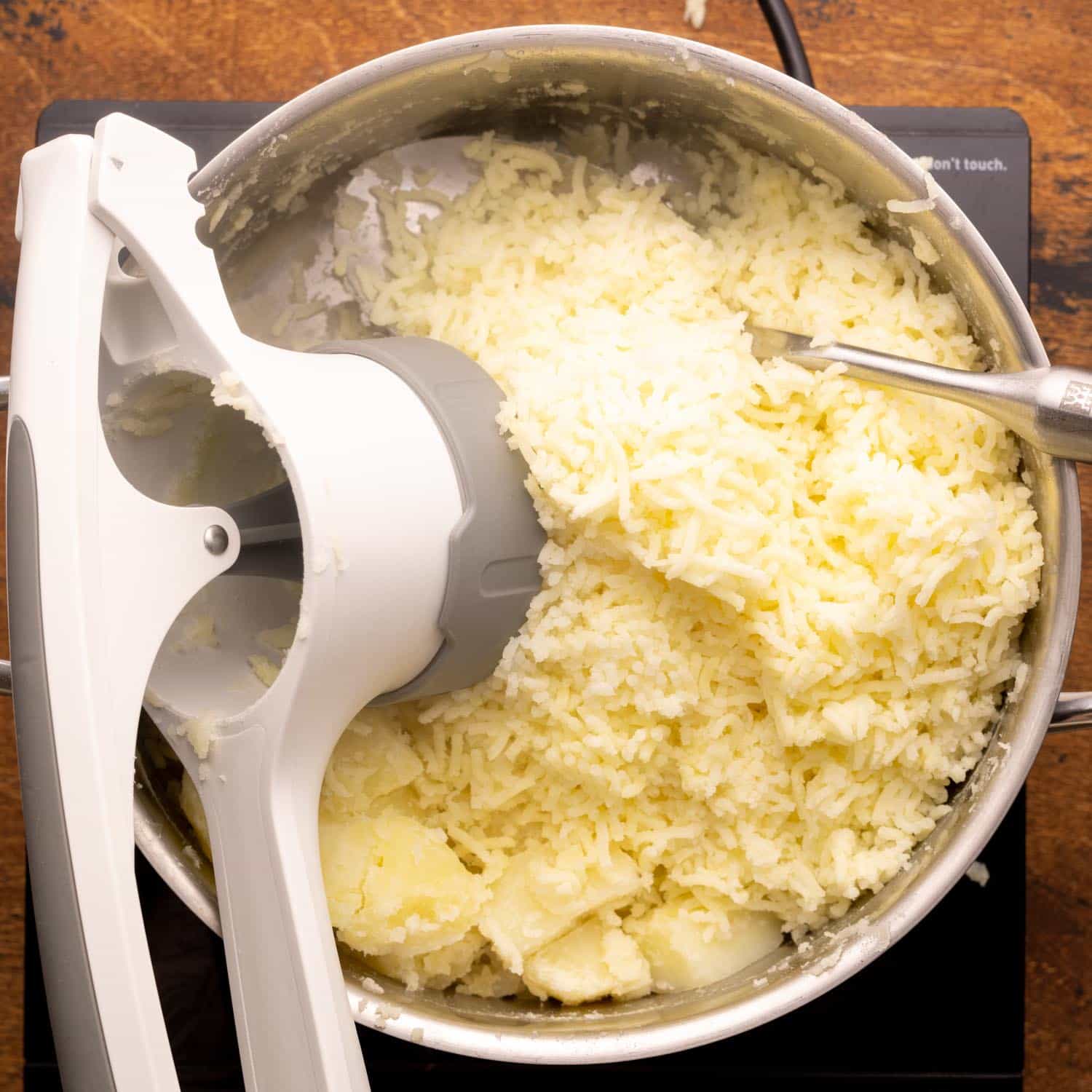 Potatoes riced into a pot using a white and gray potato ricer.