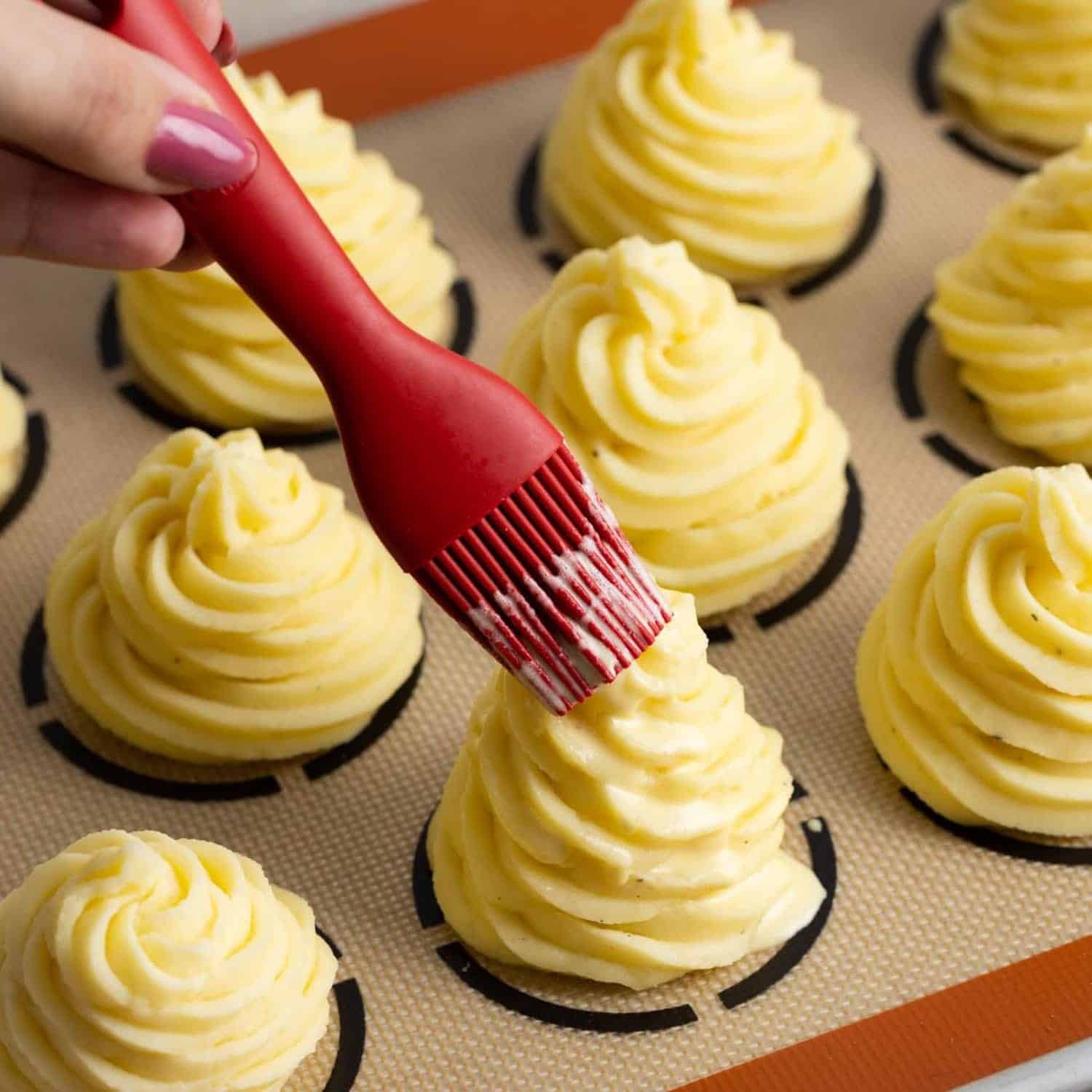 a silicone brush adding egg wash to piles of duchess potatoes.