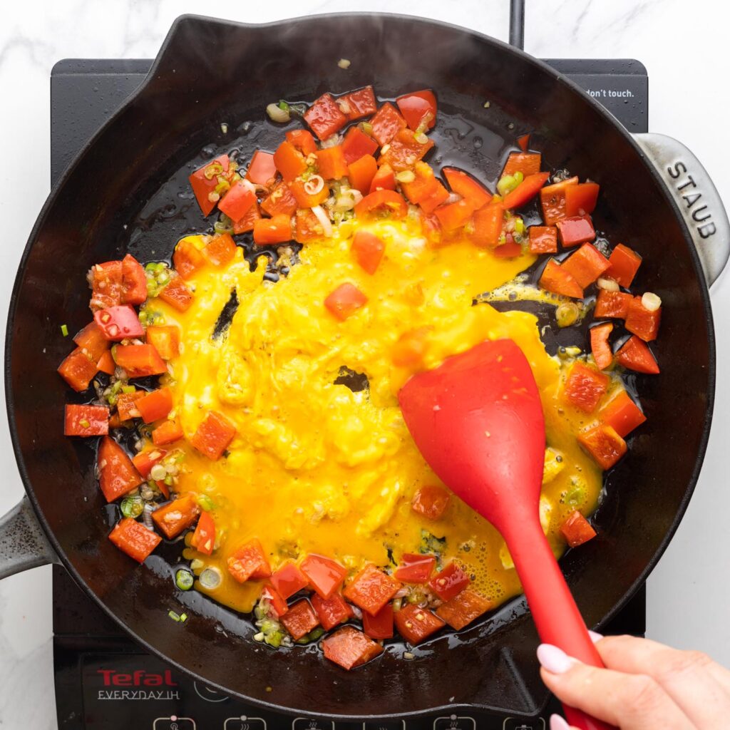 beaten egg added to a skillet of cooked peppers and onion.