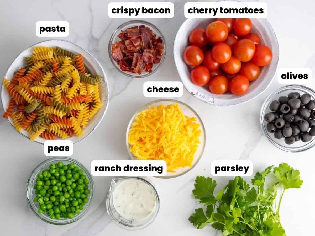 ingredients needed to make bacon ranch pasta salad with peas, olives, tomatoes, bacon, and cheese.