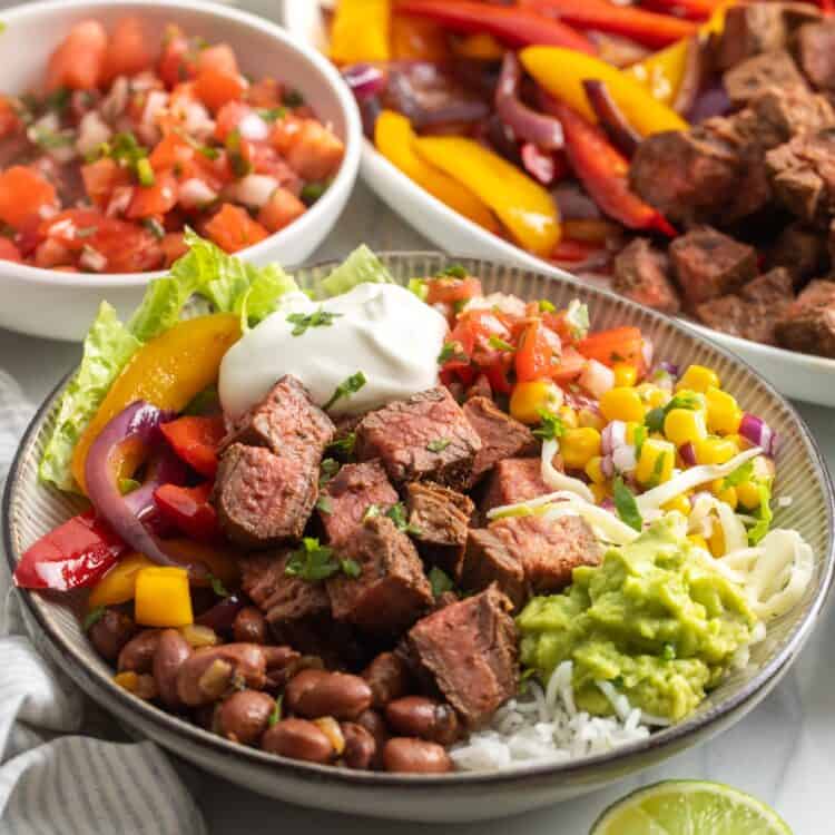 a homemade chipotle steak burrito bowl topped with sour cream, guacamole, corn, tomatoes, and cheese.