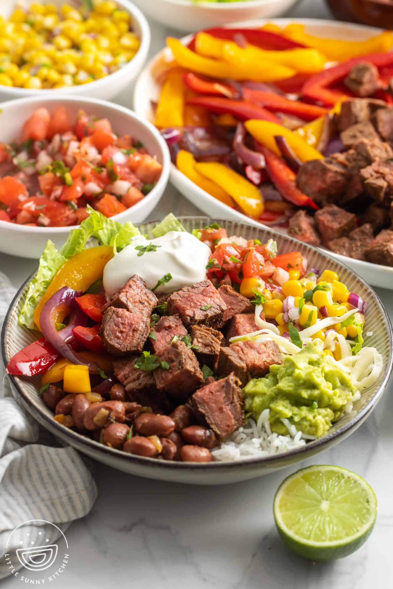 a homemade chipotle steak burrito bowl topped with sour cream, guacamole, corn, tomatoes, and cheese.