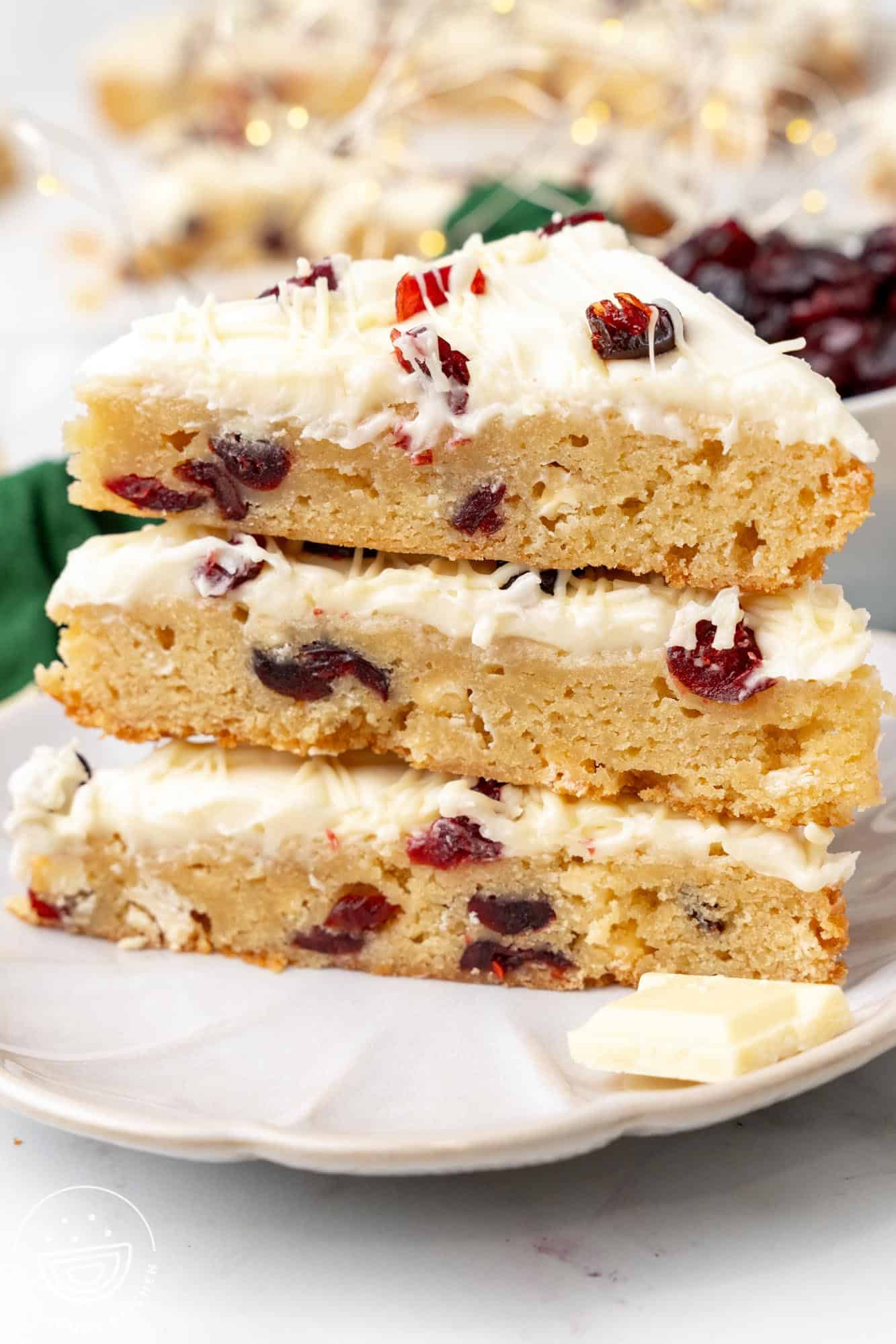 three triangle shaped cranberry bliss bars stacked on a white plate.