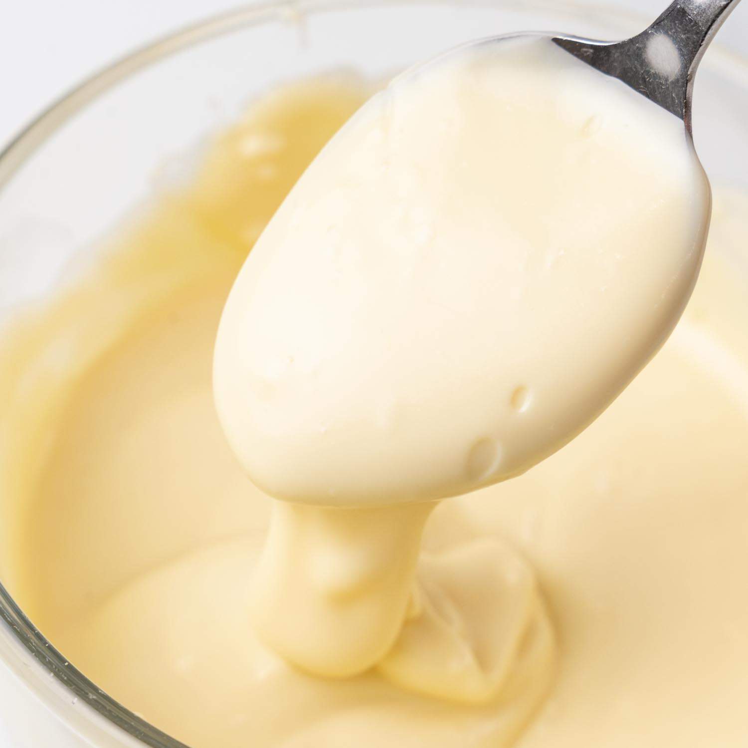 melted white chocolate falling off of a teaspoon into a bowl.