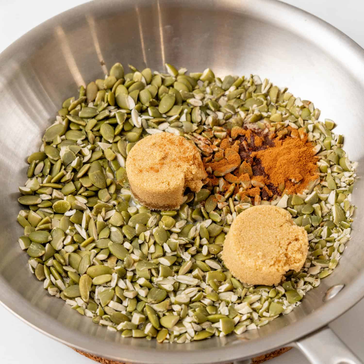 chopped raw pumpkin seeds, brown sugar, and pumpkin spice in a metal skillet.