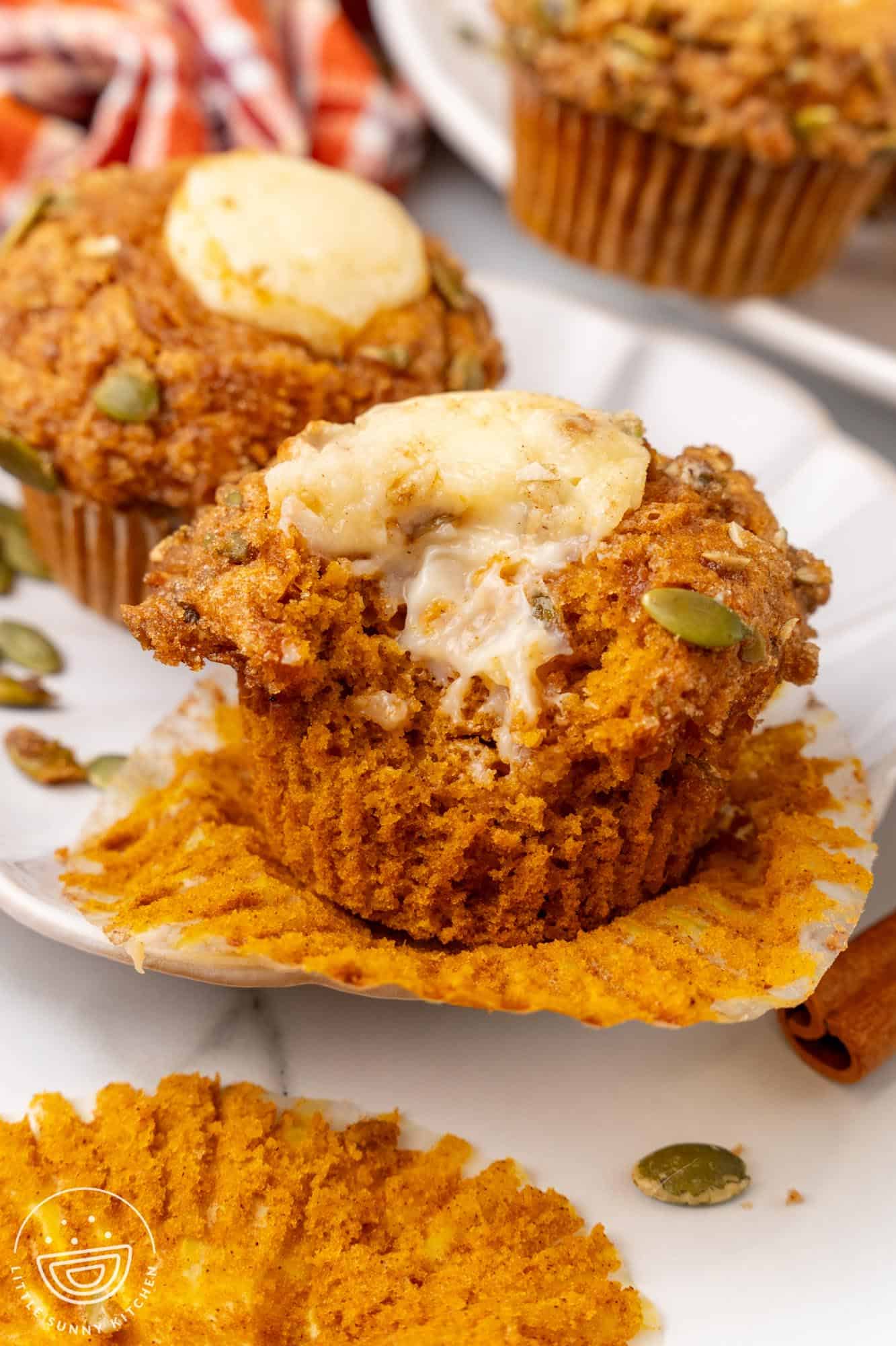 a pumpkin cream cheese muffin, removed from it's paper liner. A bite has been taken to show the creamy filling in the center.