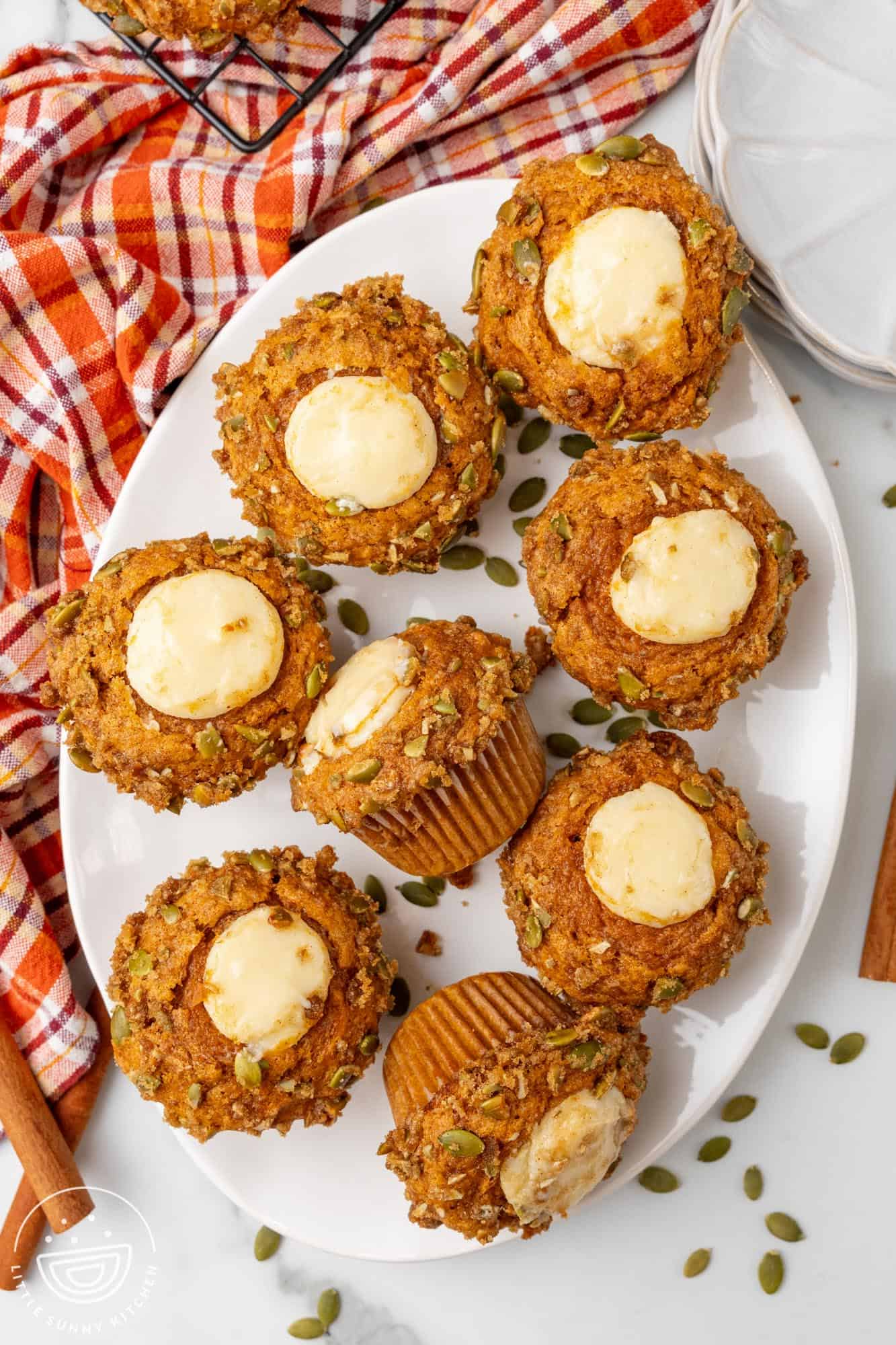 a white oval platter holding8 pumpkin muffins with raw pumpkin seeds and cream cheese filling coming out of the top.